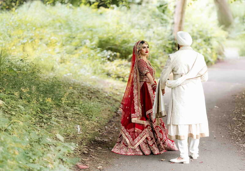 Bride looking back while walking with her groom along a leafy path