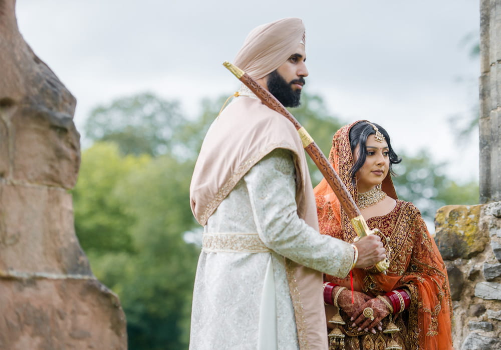 Sikh groom holding a kirpan beside the bride during their Anand Karaj wedding ceremony